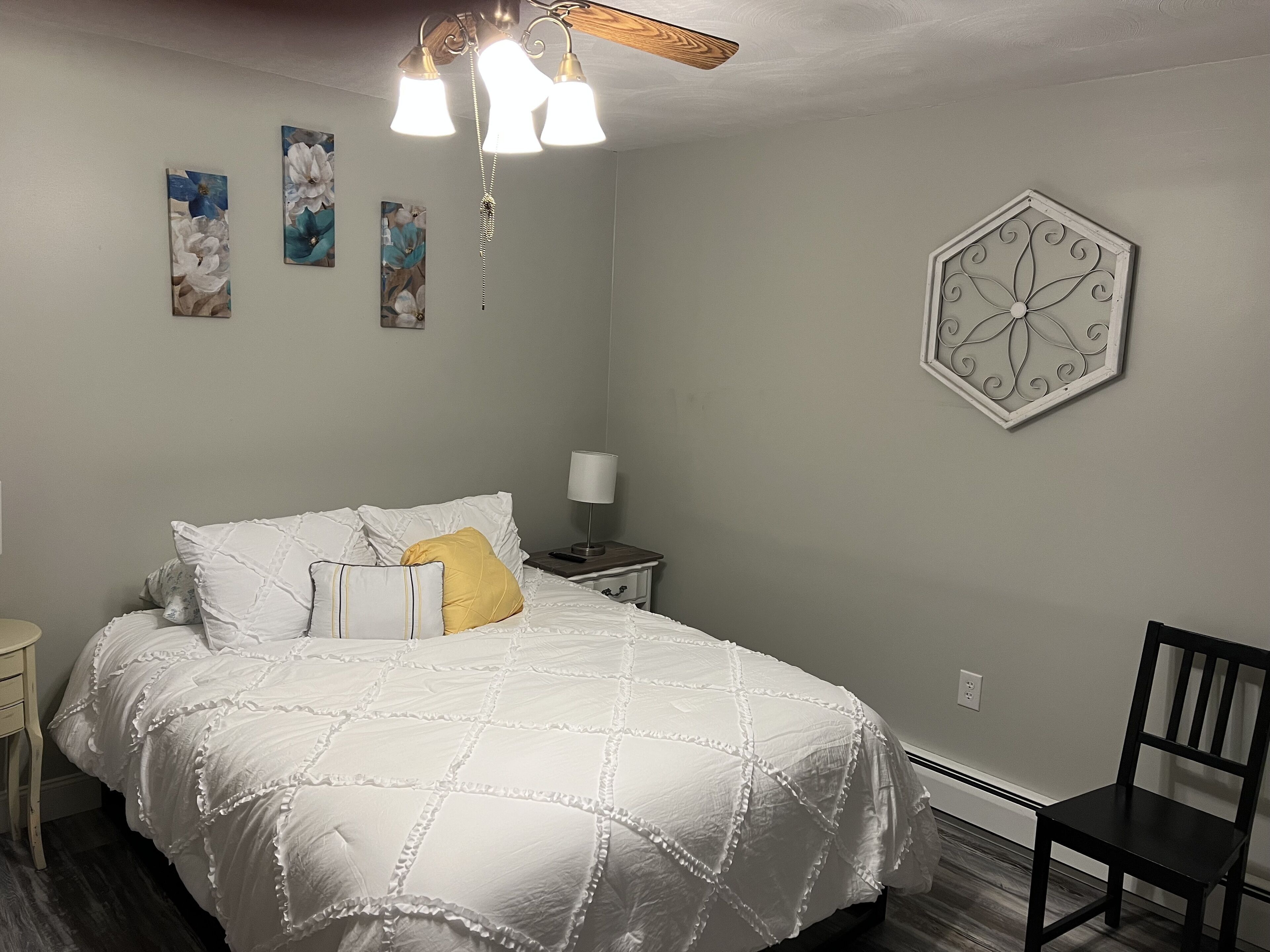 Ein Schlafzimmer mit einem Bett, einem Nachttisch, einem Sessel und Wandbildern.