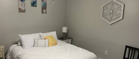 Ein Schlafzimmer mit einem Bett, einem Nachttisch, einem Sessel und Wandbildern.