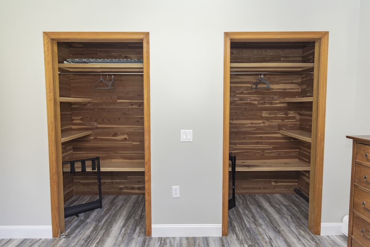 Two wooden closets with shelves and hanging rods, a dresser, and a light gray floor.