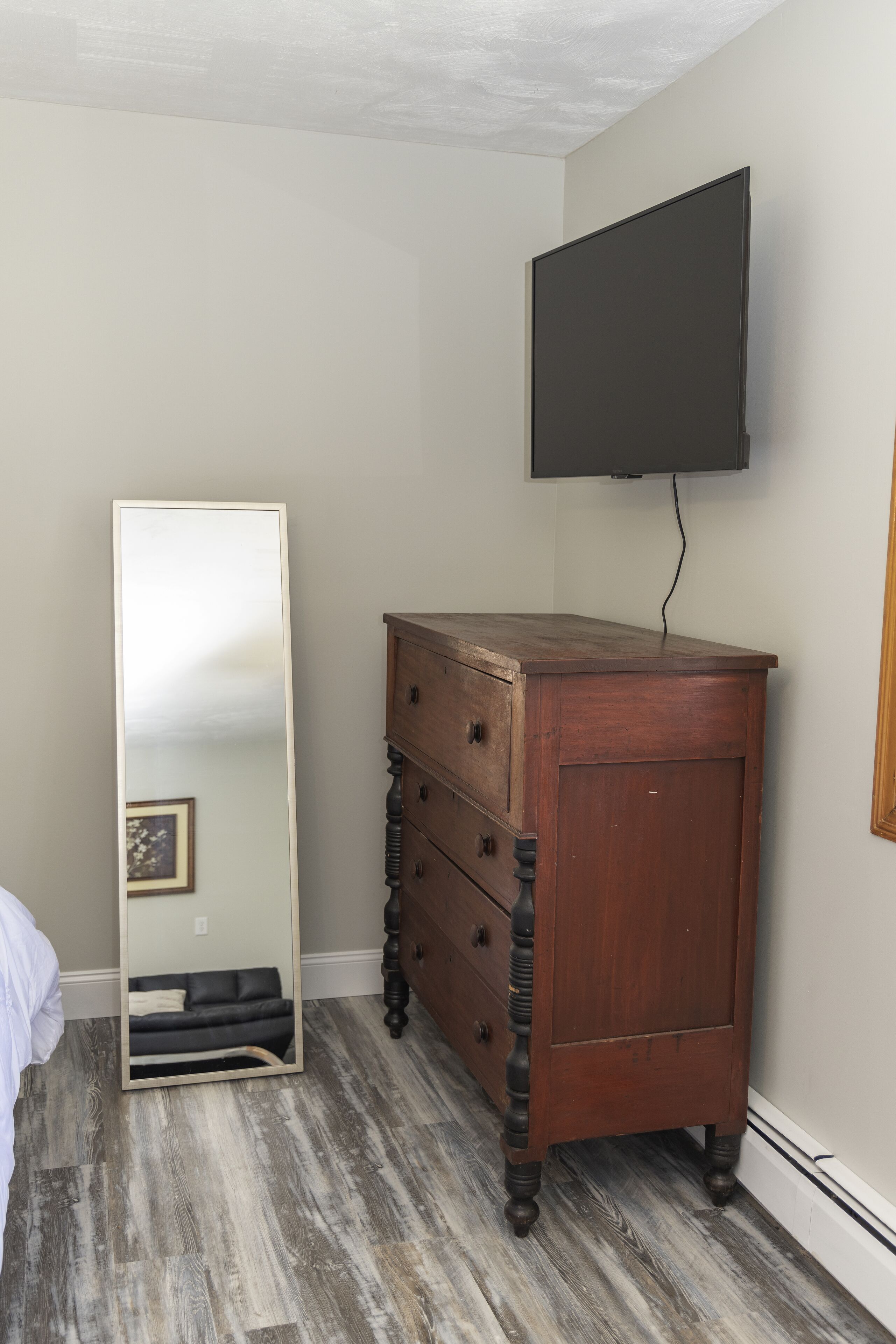 A bedroom with a wooden dresser, a large mirror, and a flat-screen TV mounted on the wall.