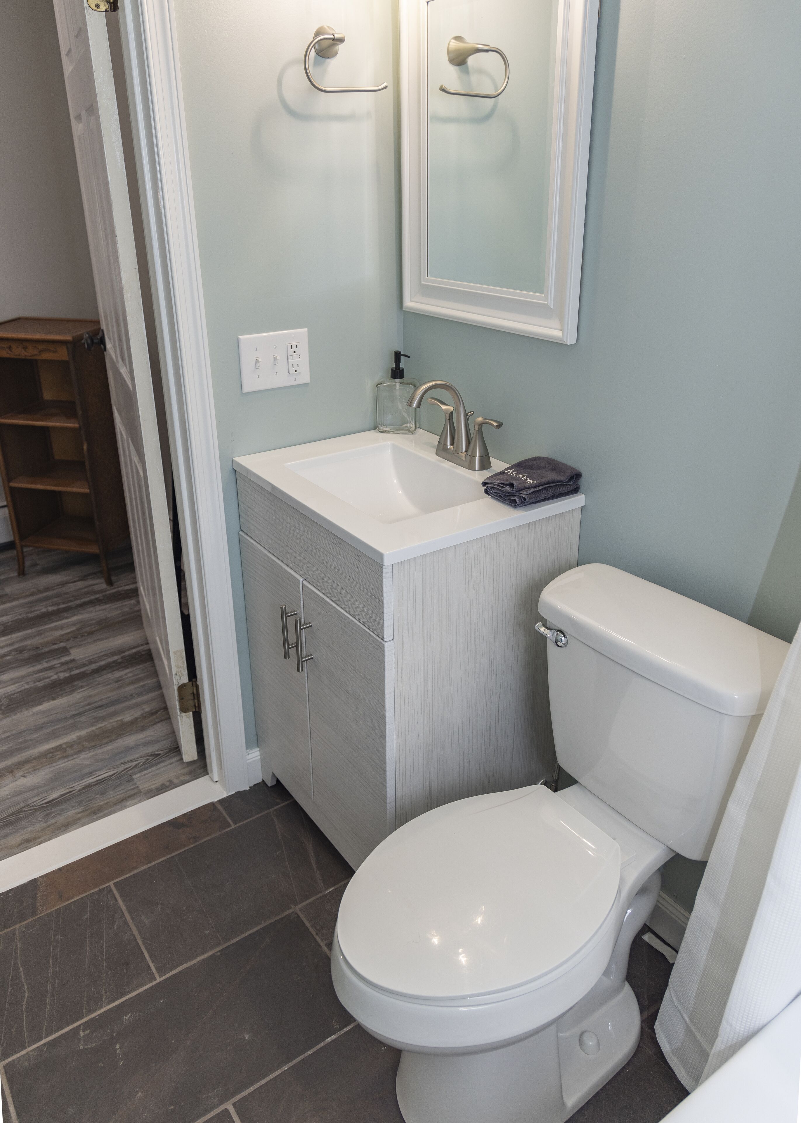A bathroom with a white toilet, a sink with a soap dispenser, and a mirror above the mirror.