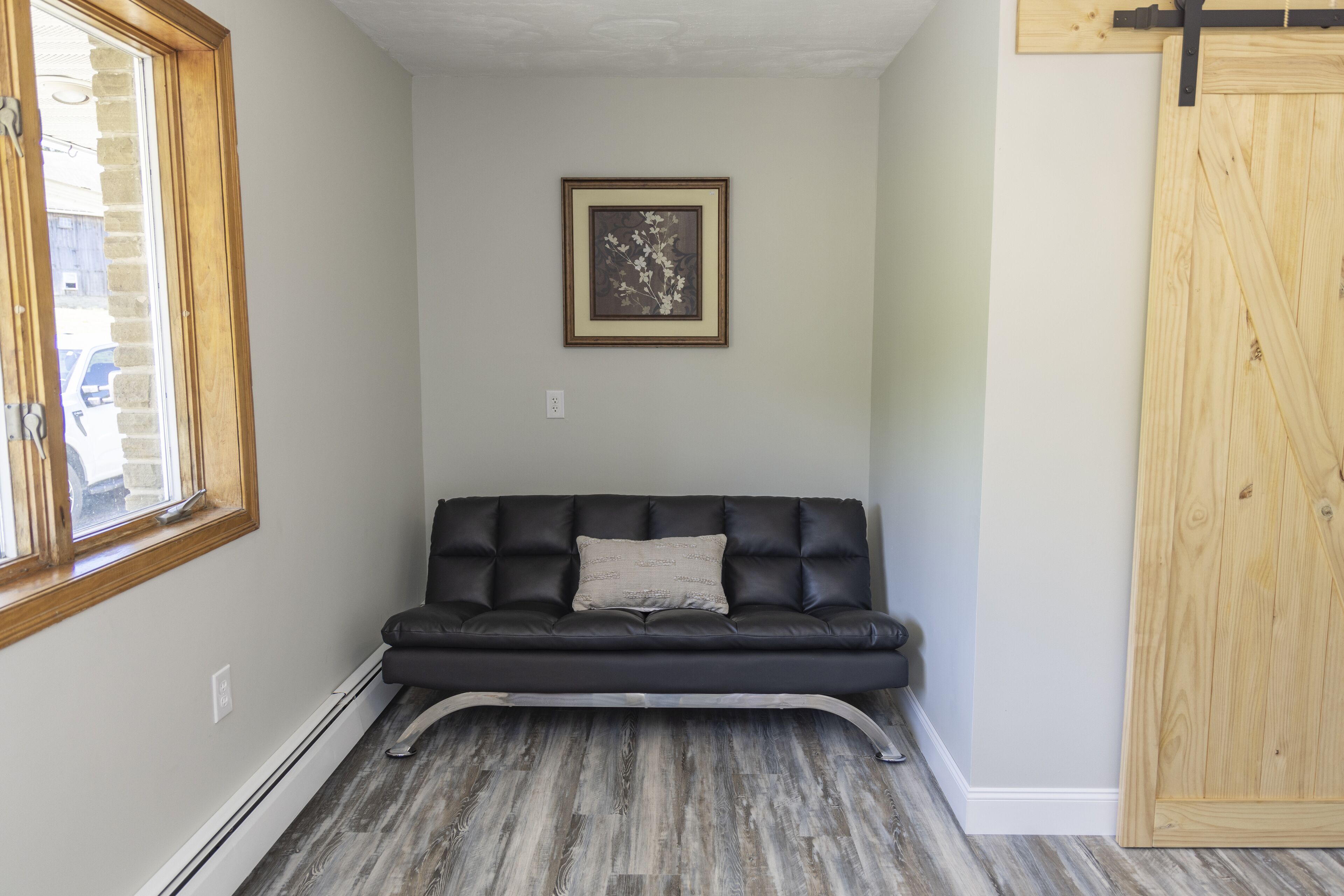 A room with a black leather sofa, a framed picture on the wall, and a wooden door.