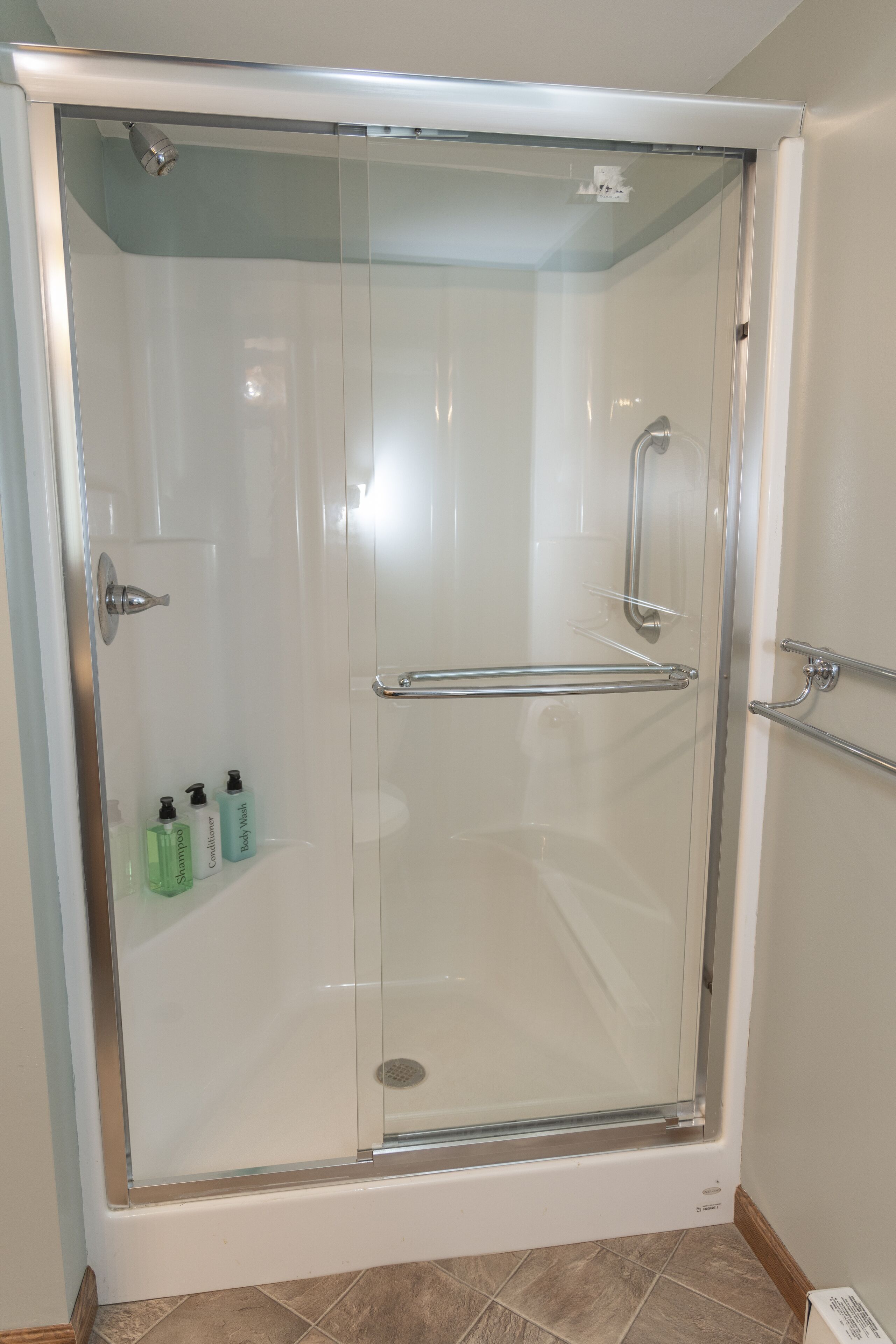 A glass-enclosed shower stall with a handheld showerhead, a handheld shower control, and a glass door.