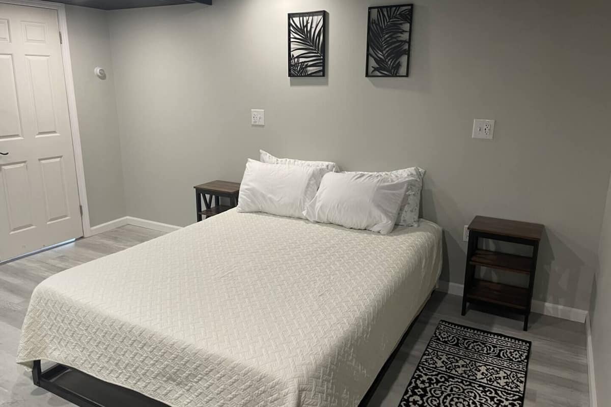 A bedroom with a bed, two nightstands, a door, and two wall-mounted decorative panels.