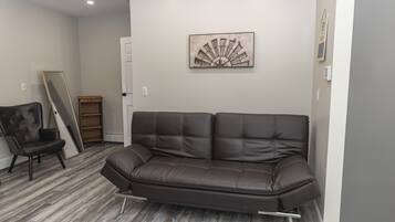 Una habitación con un sofá de cuero marrón, una silla de madera y una obra de arte colgada en la pared.