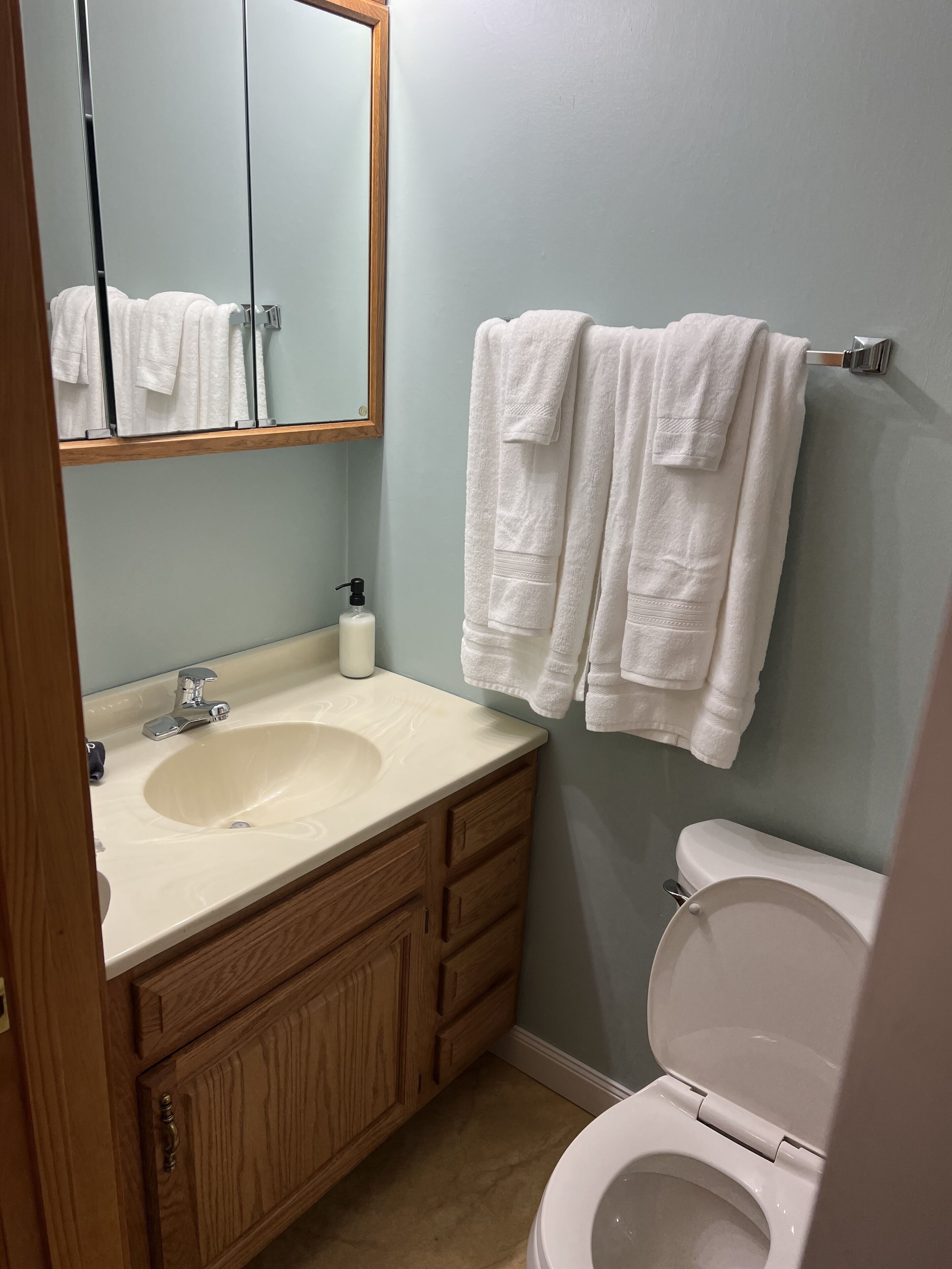 A bathroom with a wooden vanity, a sink, a mirror, and a toilet.