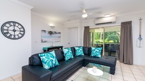 Relax in this stylish living room with a comfortable sofa, glass coffee table, and a beautiful painting of a tropical beach scene.