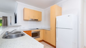 Modern kitchen with a stainless steel sink, oven, and microwave, set against a backdrop of light wood cabinetry and white granite countertops.