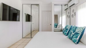 Un dormitorio con una cama grande, un televisor montado en la pared, un armario con puerta corredera y un ventilador de techo.