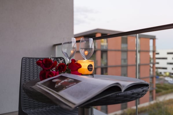 Una mesa con dos copas de vino, una vela y un ramo de rosas rojas en un balcón con vista a edificios.