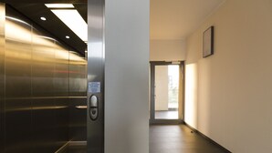 An elevator interior with a metallic finish, a control panel, and a corridor leading to a door with a view outside. - Villa Doria  (Luxembourg City)