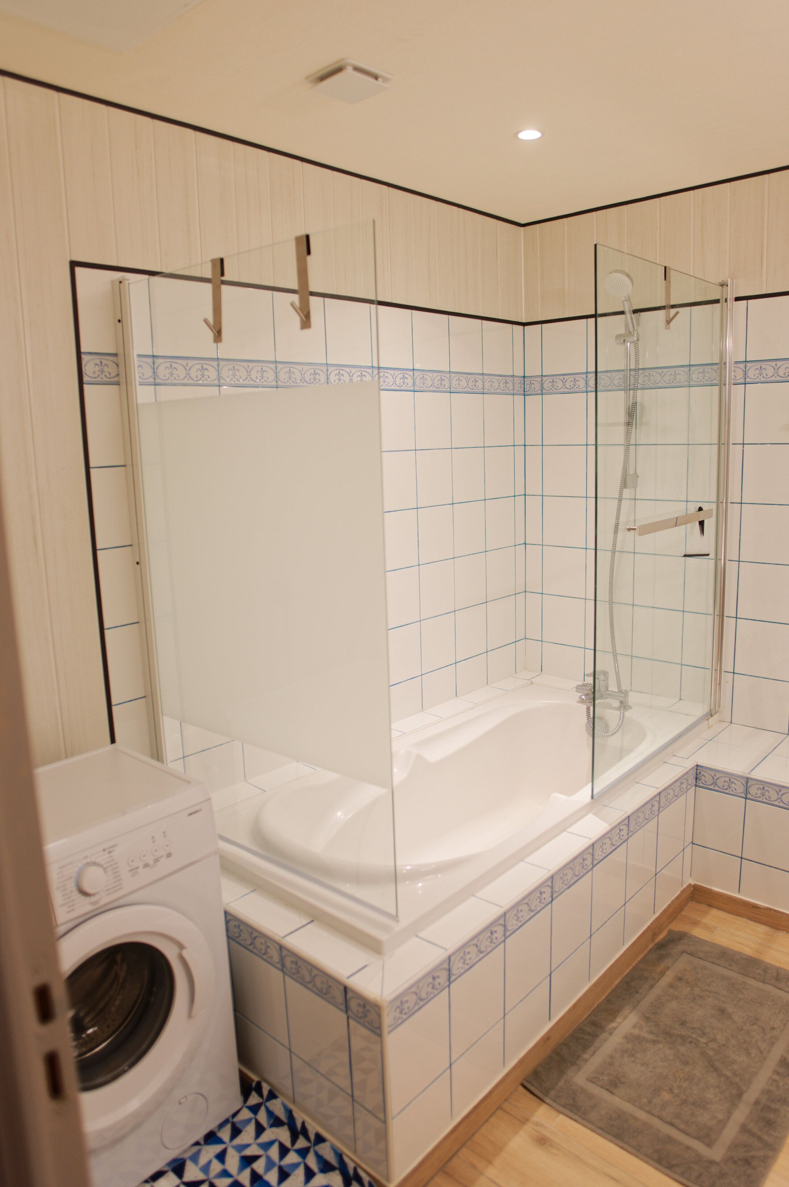 Une salle de bain avec une douche à parois de verre, une baignoire blanche et un lave-linge.