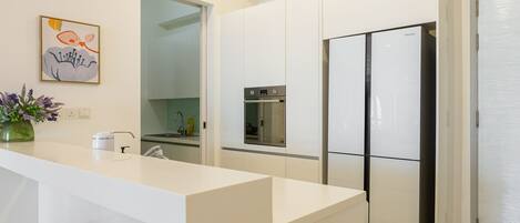 A modern kitchen with white cabinetry, a stainless steel refrigerator, and a built-in oven.