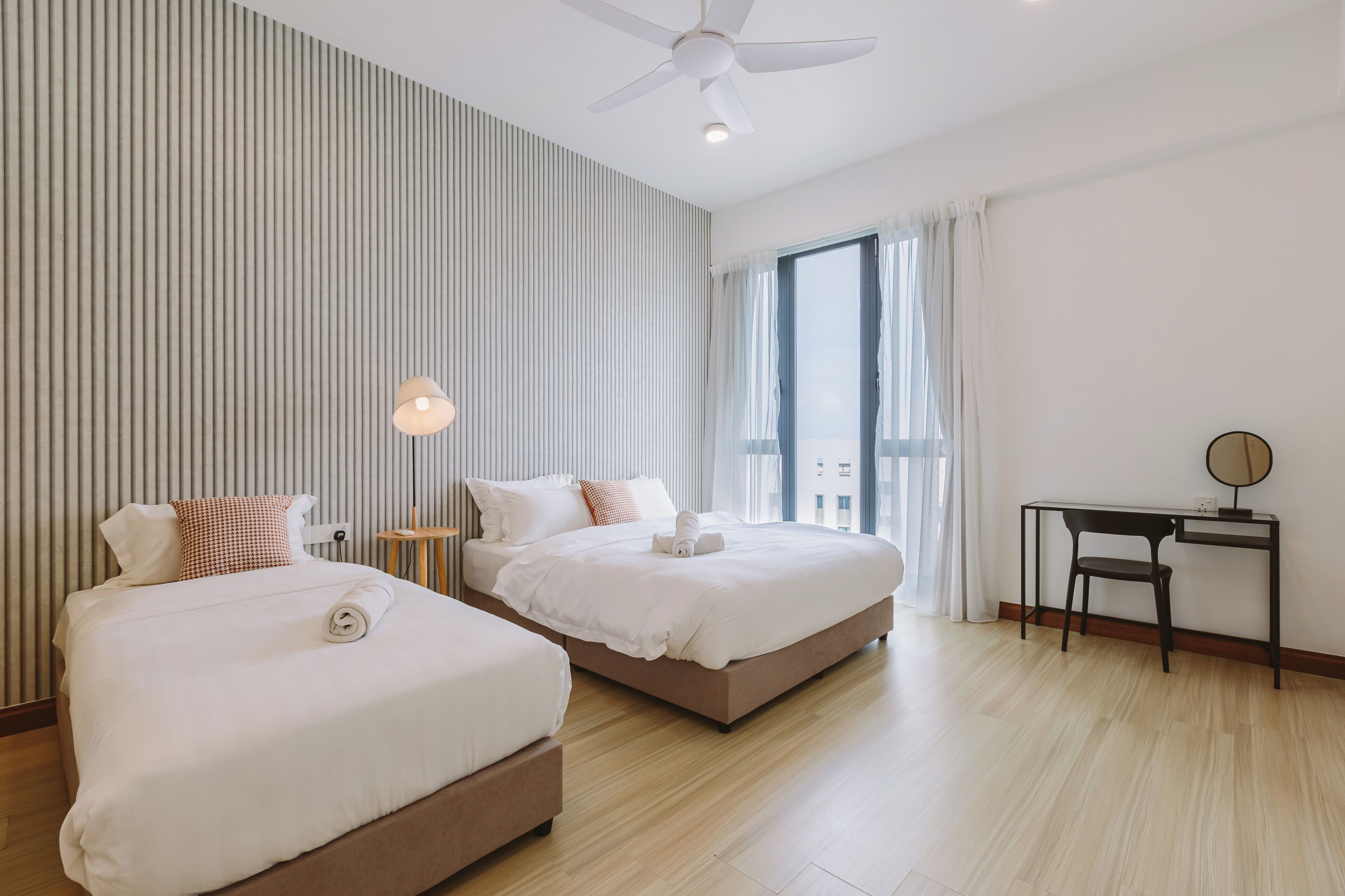 Une chambre d’hôtel avec deux lits, un bureau, une chaise, un ventilateur de plafond et une grande fenêtre avec des rideaux.