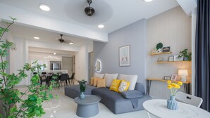 A modern living room with a grey sofa, a white coffee table, and a dining area in the background. - The Jazz Serviced Suites (George Town)