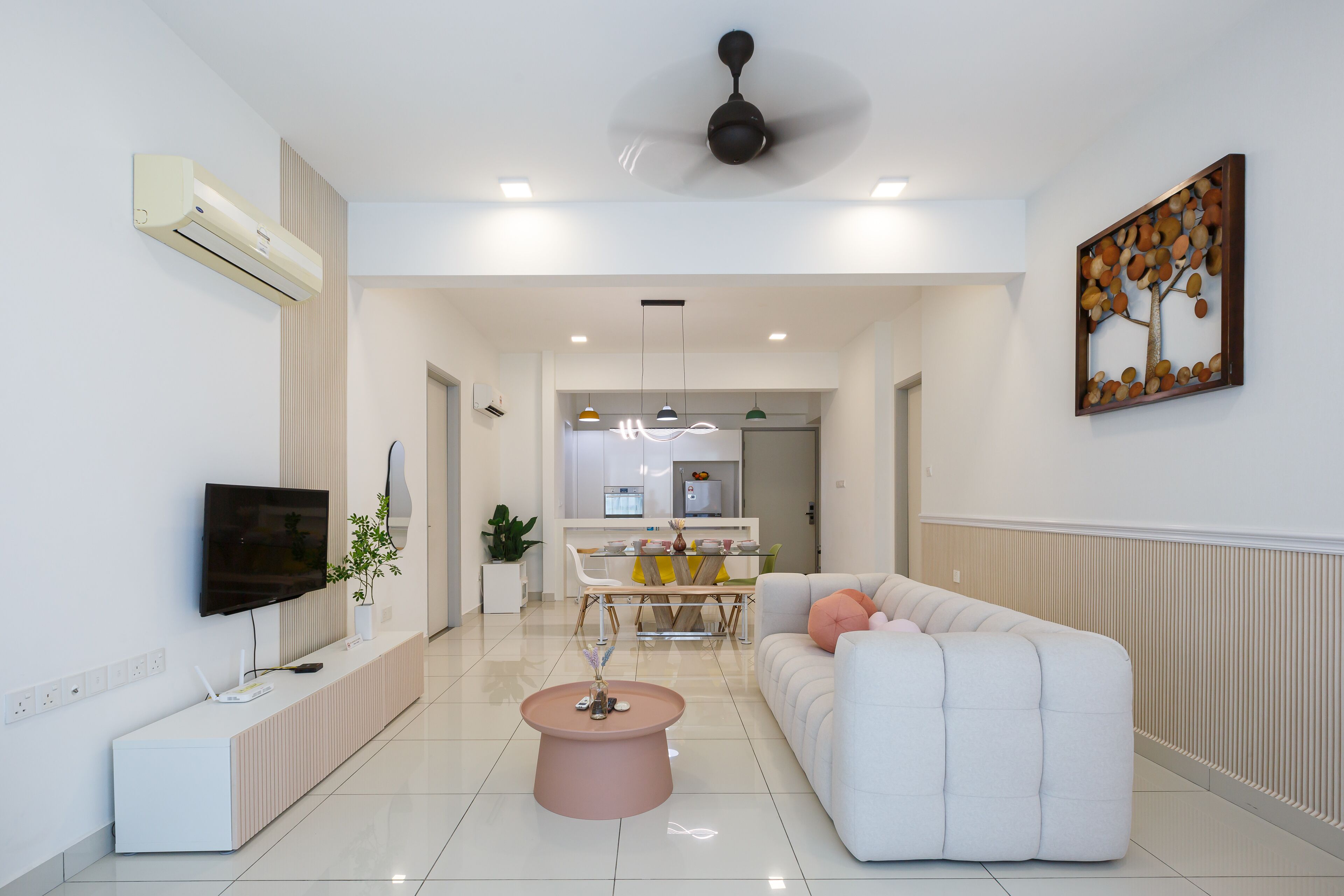 Uma sala de estar moderna com um sofá branco, uma mesa de centro rosa e uma televisão de tela plana na parede.