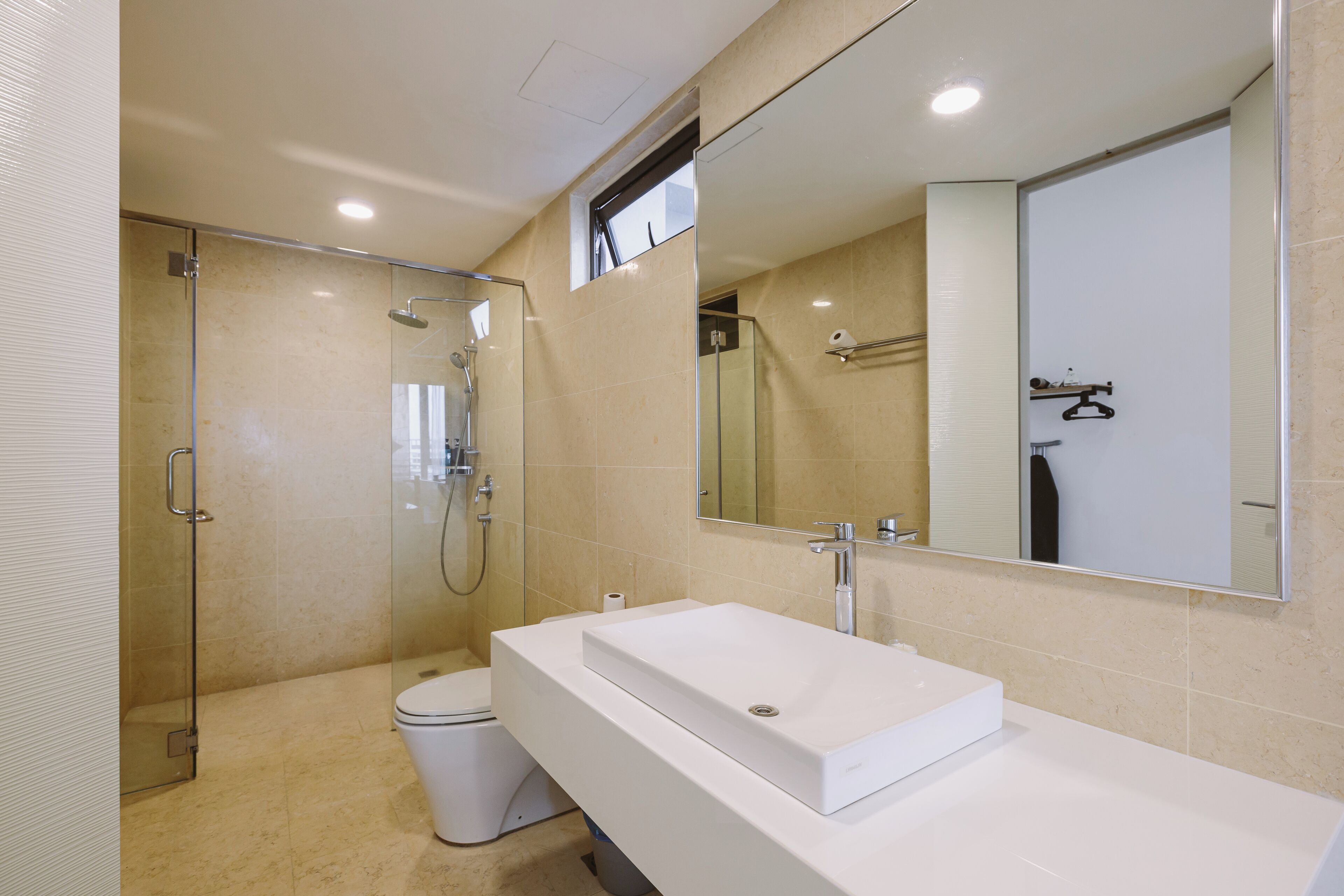 Een moderne badkamer met een douchecabine van glas, een wit wastafeltje en een grote spiegel.