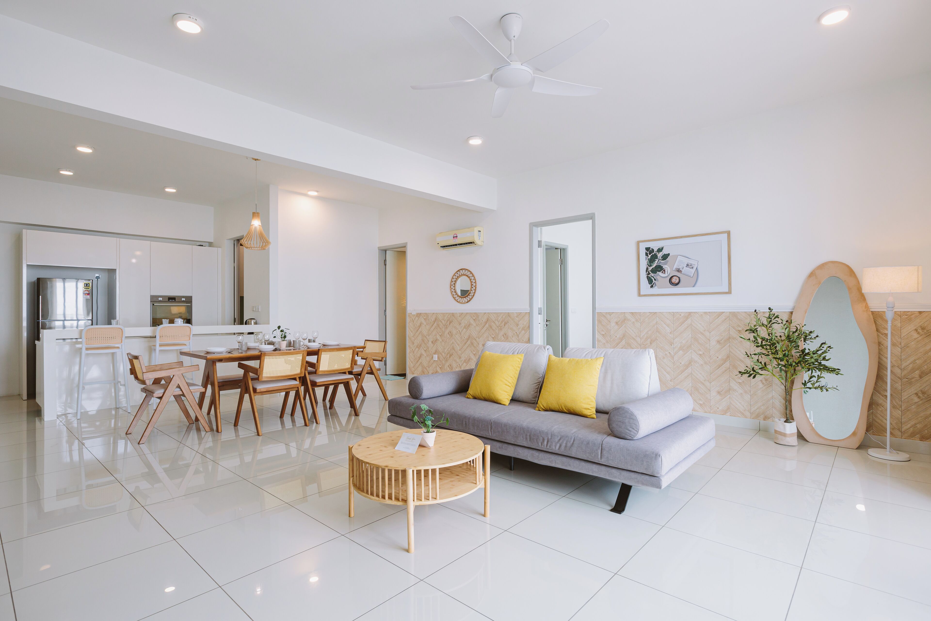 A modern living room with a grey sofa, wooden coffee table, and a dining area with a white table and chairs.