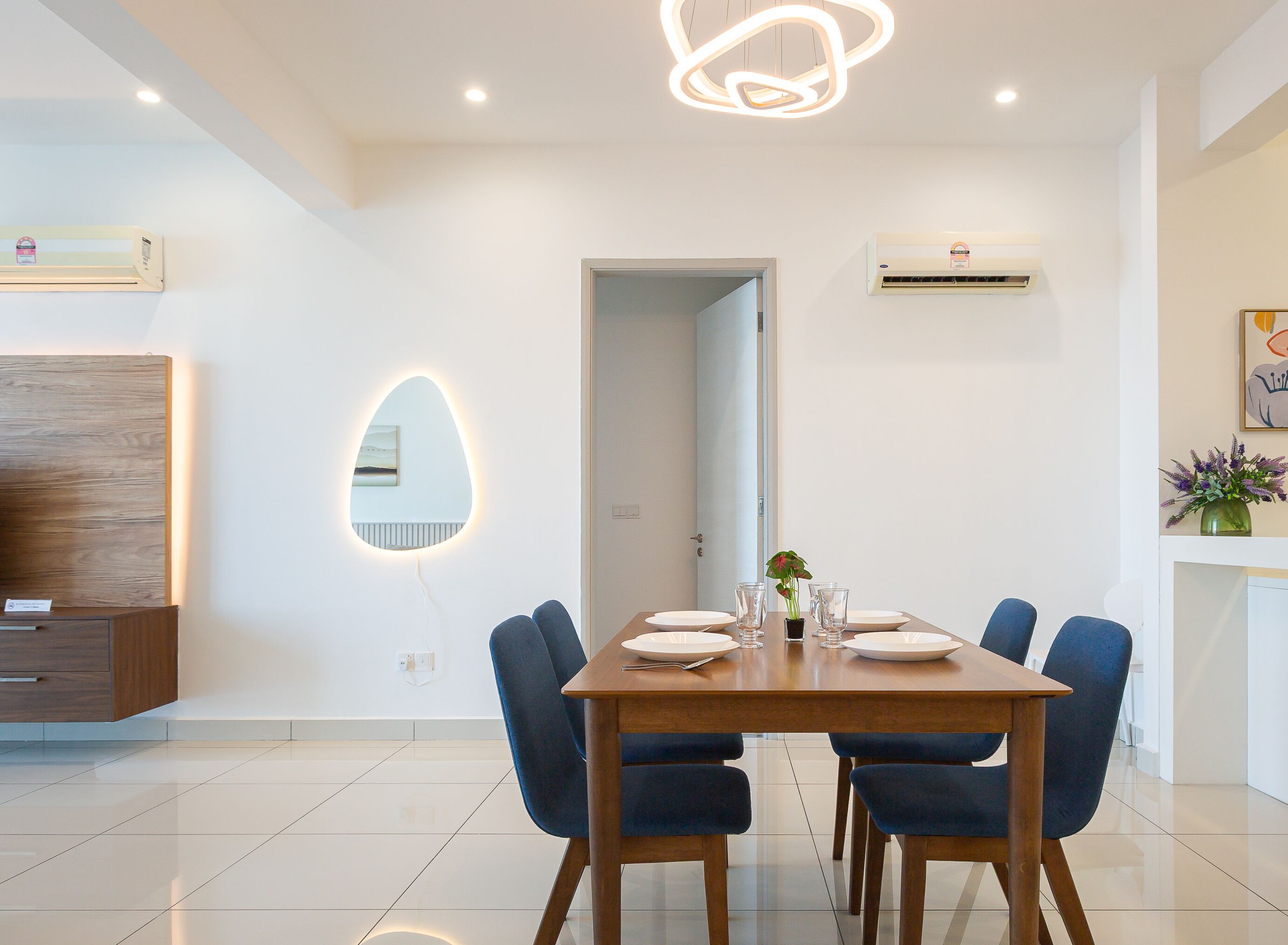 A modern dining area with a wooden table, six blue chairs, and a unique wall-mounted light fixture.