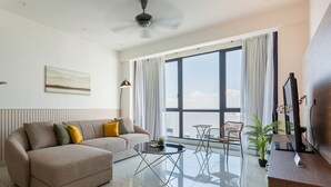 A modern living room with a sofa, coffee table, and chairs. There is a large window with curtains, a ceiling fan, and a plant. - The Jazz Serviced Suites (George Town)