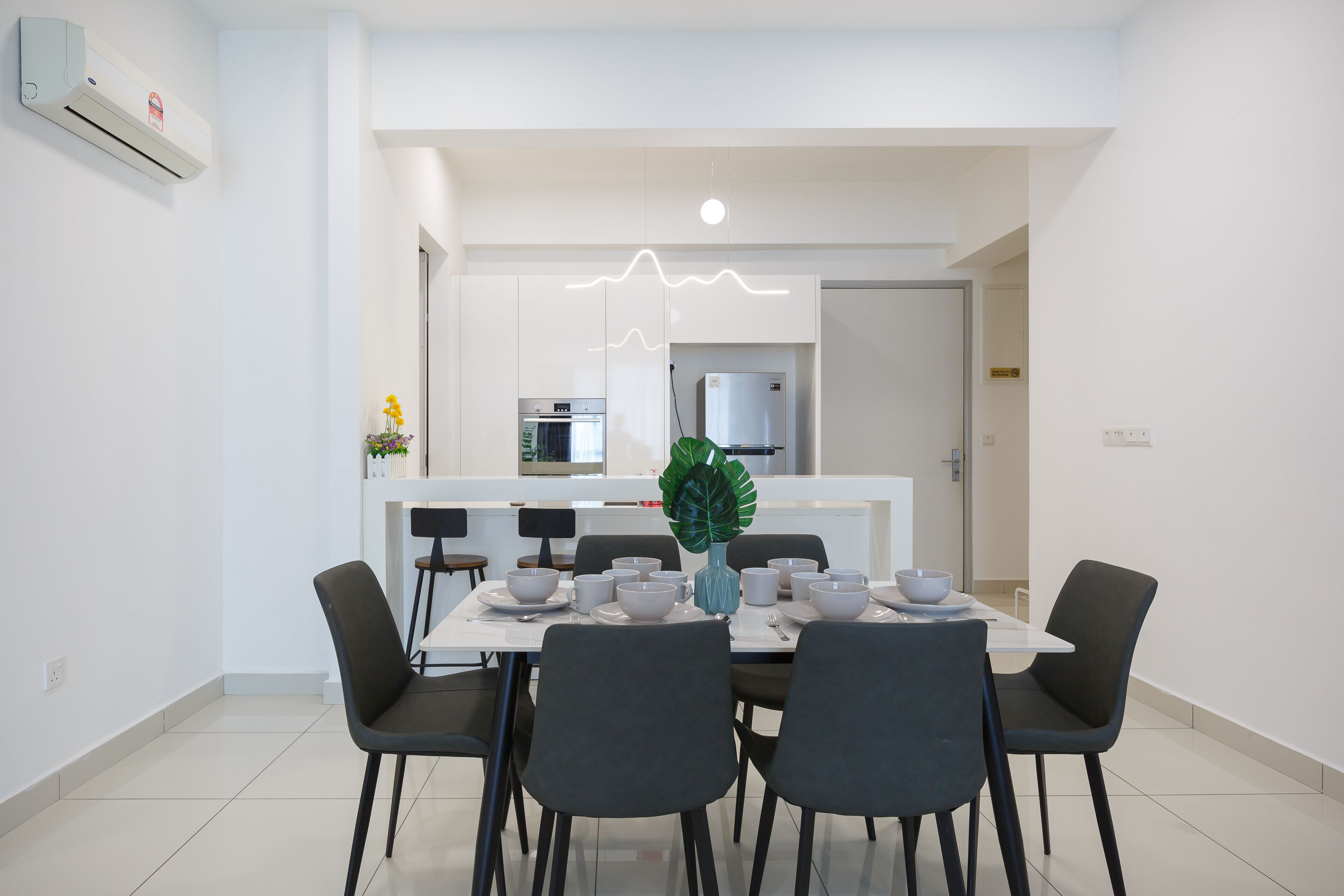 A modern dining area with a white table, black chairs, and a decorative plant.