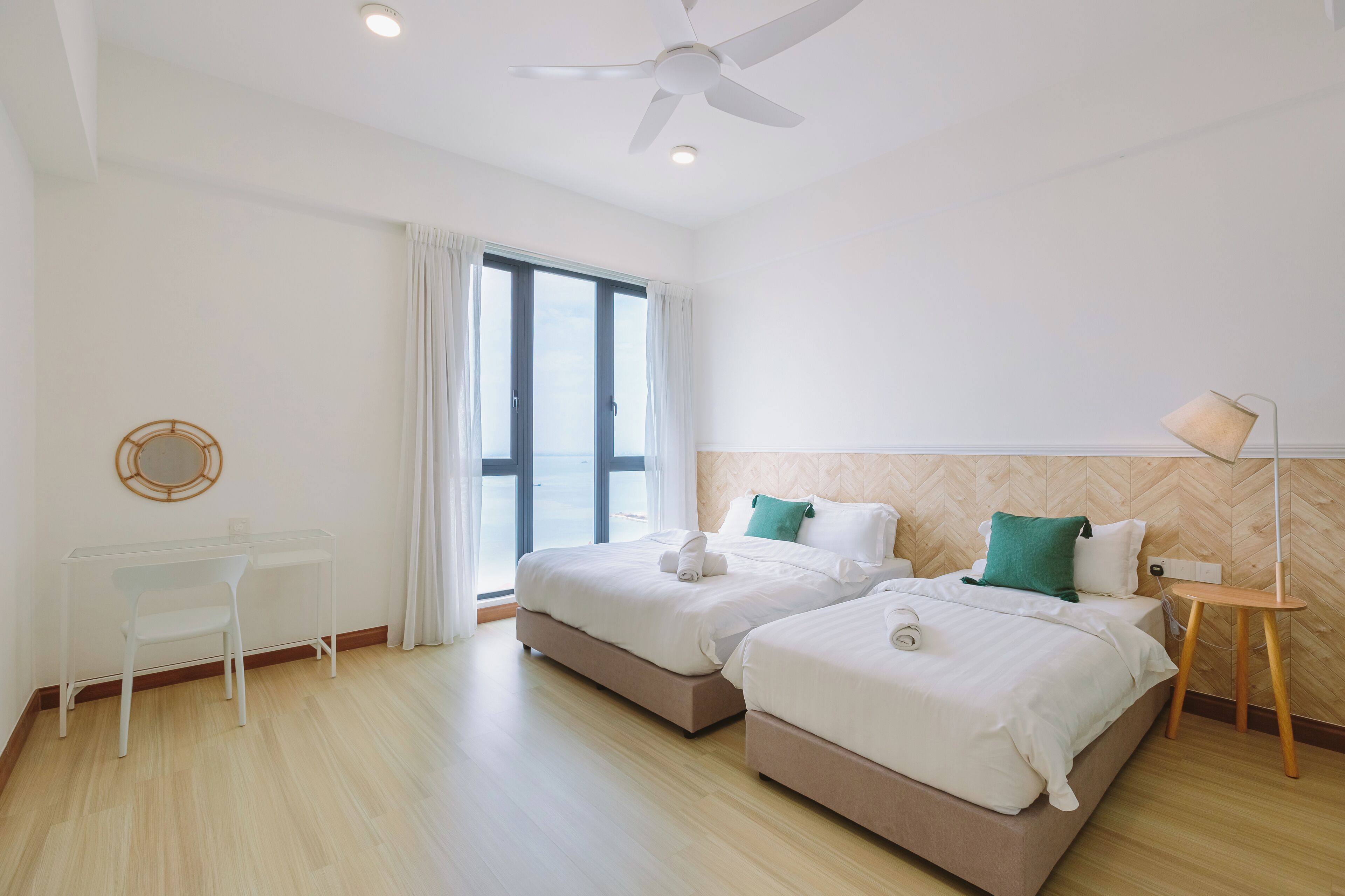 A hotel room with two beds, a desk, a chair, a lamp, and a ceiling fan.