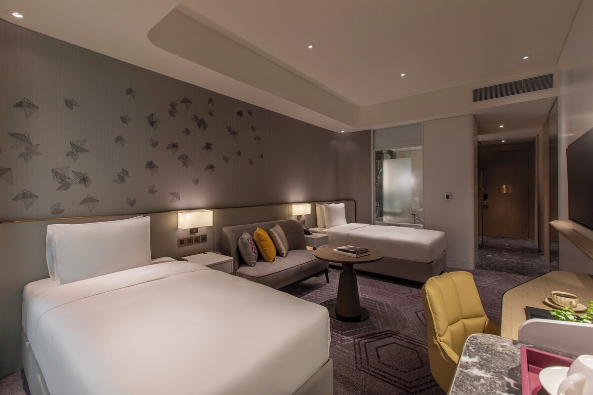 Una habitación de hotel moderna con dos camas, un sofá, una mesita y una silla.