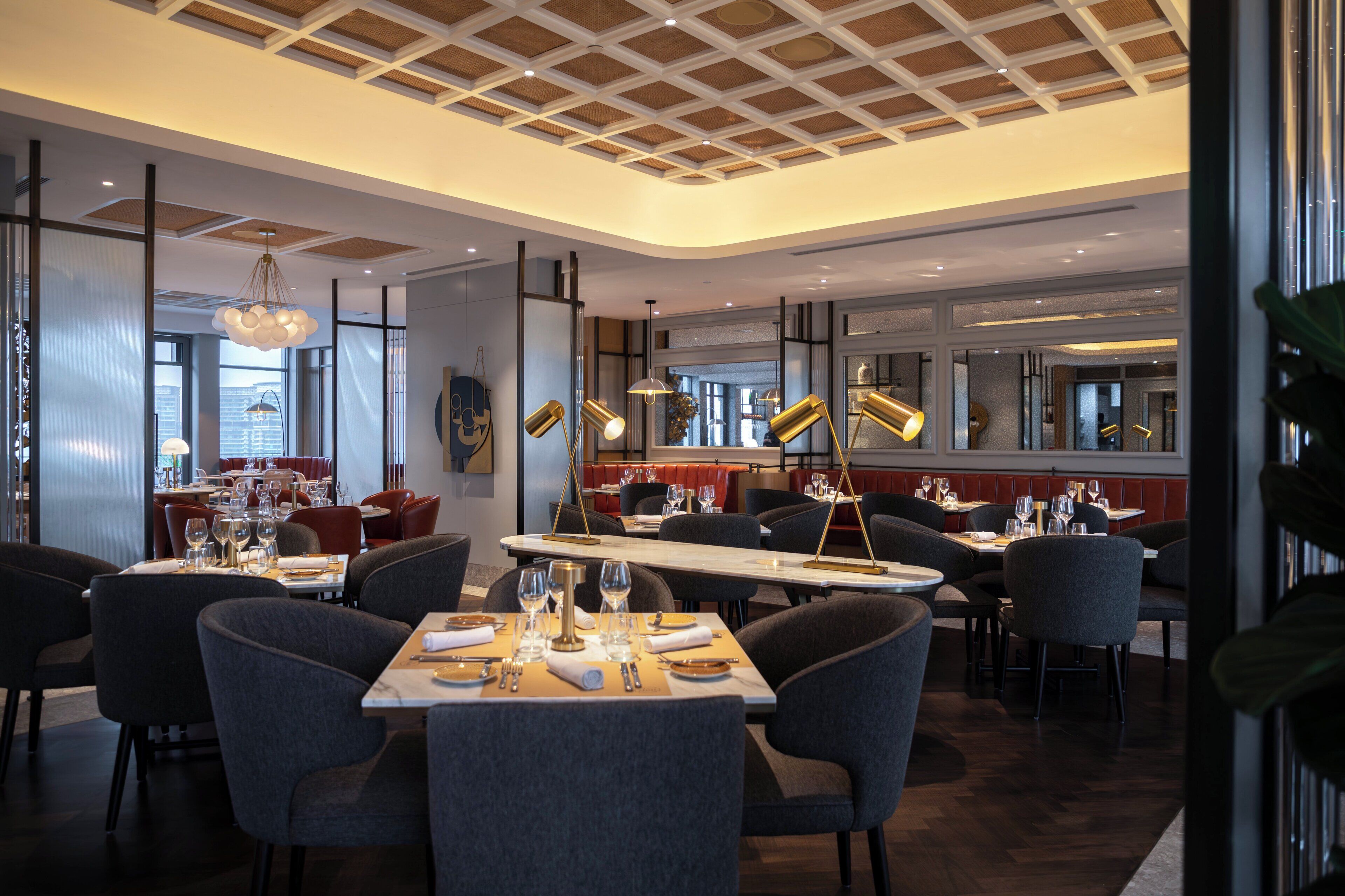 Ein modernes Restaurant mit hoher Decke, großen Fenstern und zeitgemäßer Einrichtung.