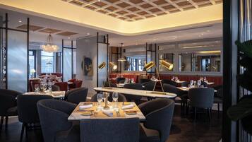 Ein modernes Restaurant mit hoher Decke, großen Fenstern und zeitgemäßer Einrichtung.