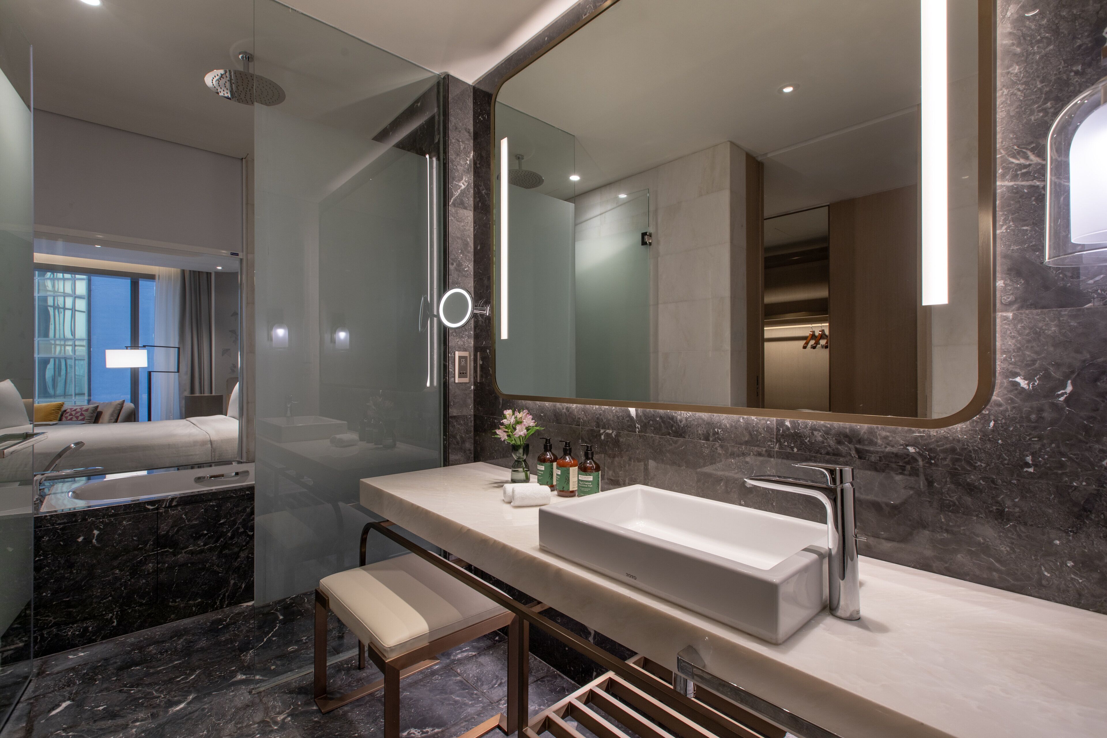 Une salle de bain moderne avec un grand miroir, un lavabo blanc et un banc.