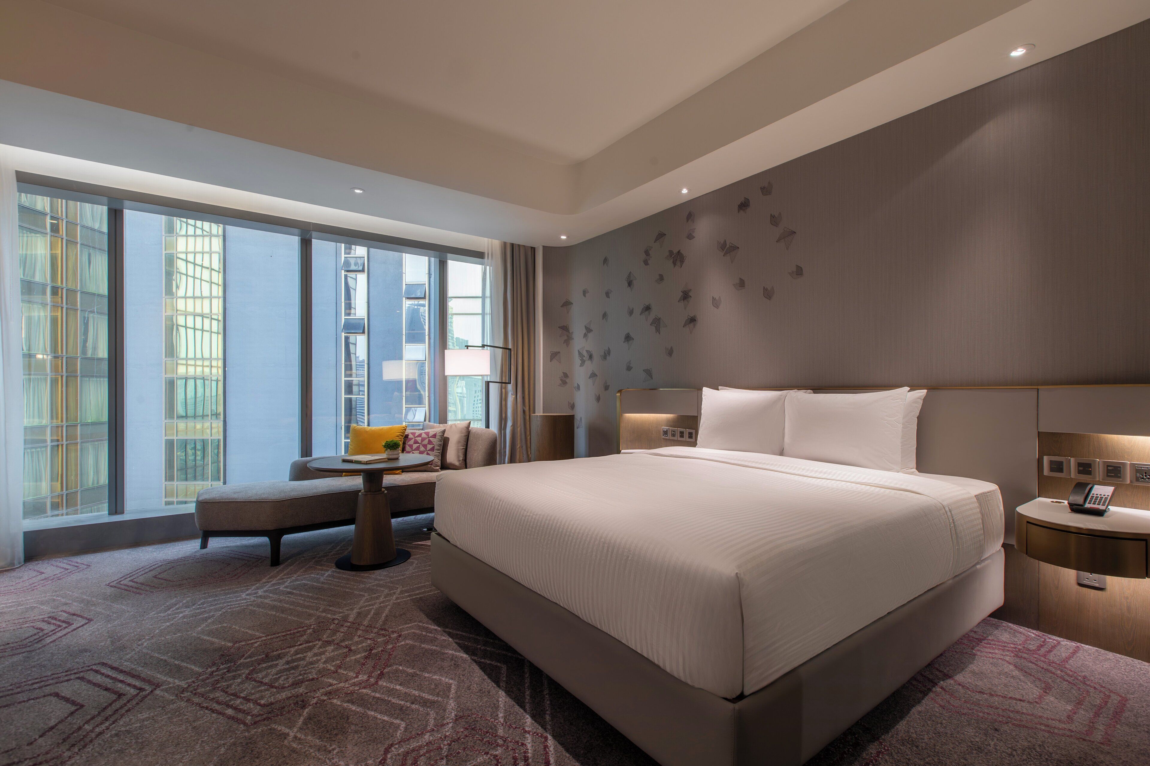 A modern hotel room with a large bed, a seating area, and a view of the city.