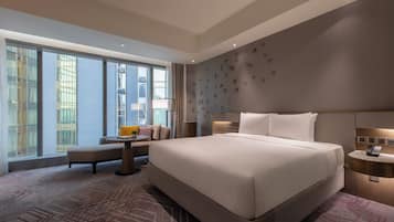 A modern hotel room with a large bed, a seating area, and a view of the city.