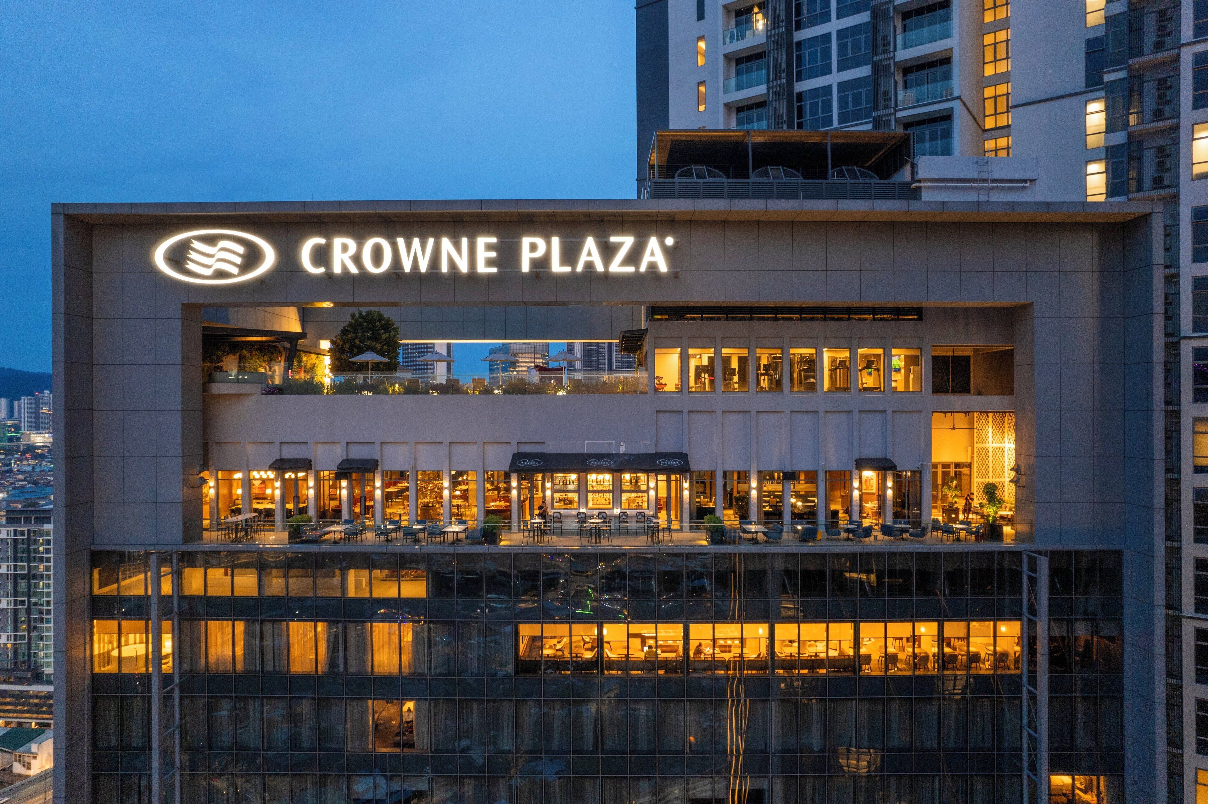 Un bâtiment moderne portant l’enseigne « CROWNE PLAZA », indiquant un espace commercial à plusieurs niveaux, avec des zones d’assise bien visibles.