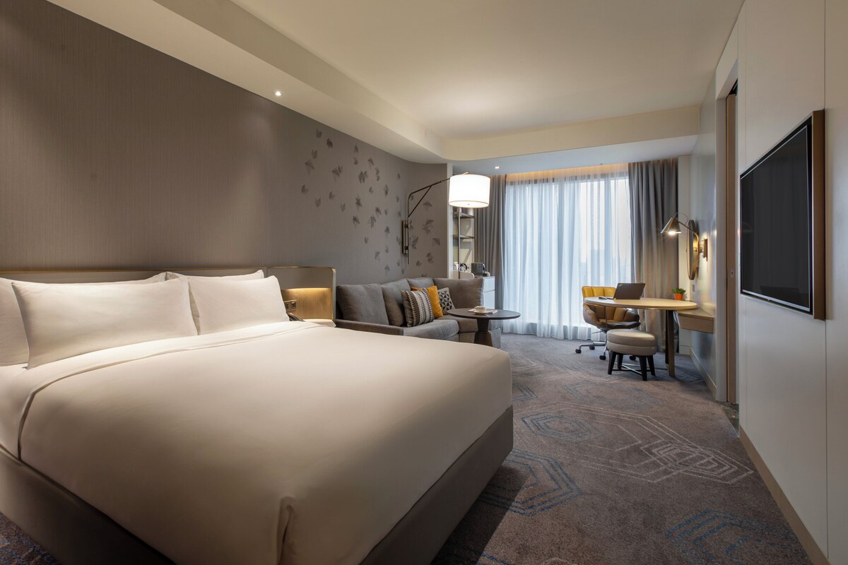 Una habitación de hotel con una cama grande, un escritorio con una computadora portátil, una silla y un televisor.