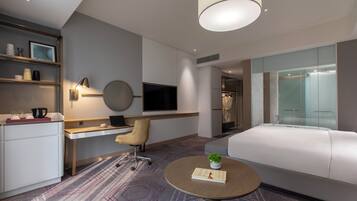A modern hotel room with a desk, chair, bed, and a small round table with a book.