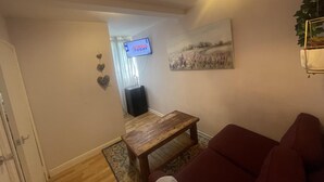Een woonkamer met een houten salontafel, een rode bank, een aan de muur bevestigde televisie en een schilderij erboven.
