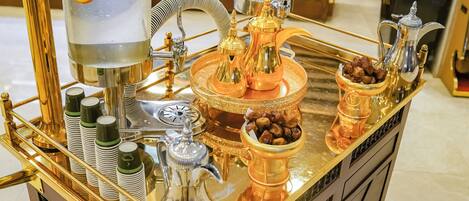 Ein luxuriöser Getrännewagen mit goldener Oberfläche, der einen Wasserhahn, eine Kaffeekanne und eine Schale mit Nüssen und eine Zuckerdose präsentiert.