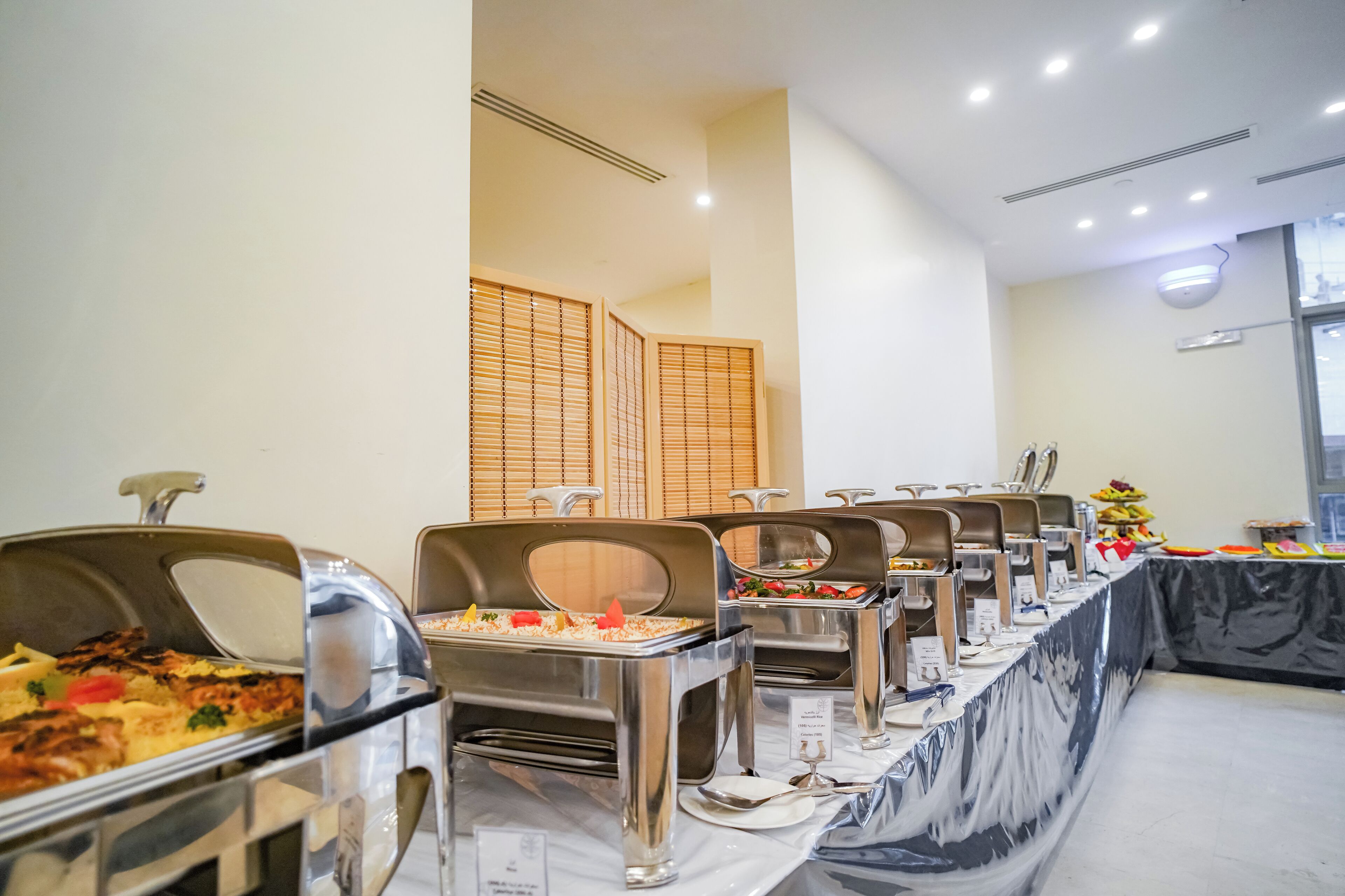 A buffet setup with multiple serving stations, a marble tablecloth, and a window with blinds in the background.