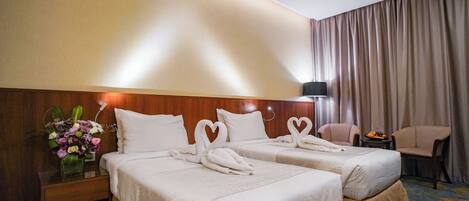 A hotel room with two beds, a nightstand with a vase of flowers, a chair, and a small table with fruit.