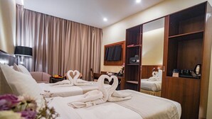 Habitación de hotel con dos camas, un armario, un escritorio, una silla, un televisor y una ventana con cortinas.