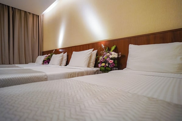 Habitación de hotel con tres camas, cortinas color beige y un arreglo floral en la cabecera.