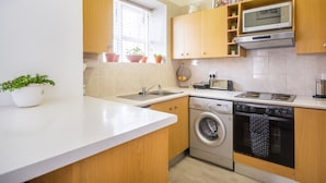 A modern kitchen with a built-in washing machine, a microwave, and a toaster. There are wooden cabinets and a window with blinds.