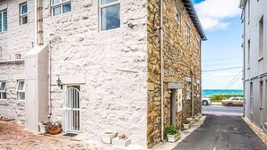 A narrow street with a stone building on the left and a view of the sea on the right.
