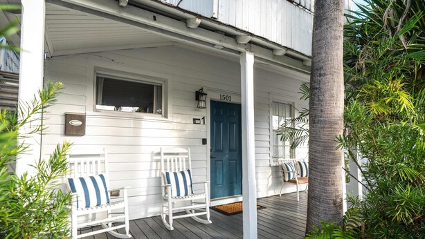 Een wit houten veranda met twee schommelstoelen, een blauwe deur en een bord met het nummer 1501.