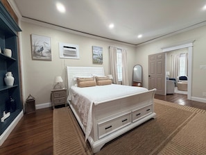 A bedroom with a large bed, bedside tables, a wardrobe, a mirror, and a door leading to another room.
