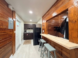 A compact kitchen with wooden walls, a refrigerator, a coffee maker, and a television mounted on the wall.