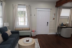 A living room with a sofa, a round coffee table, a door, and a small table with a lamp.