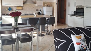 Una cocina moderna con una isla central, un comedor con sillas y un sofá con un cojín estampado.