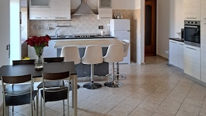 Una cocina moderna con armarios blancos, una isla central con taburetes y un horno empotrado, además de una lámpara colgante.