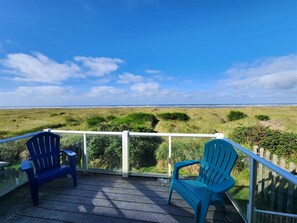 A wooden deck with two blue Adirondack chairs overlooking a grassy landscape and the ocean. - Las Brisas- Beautiful Views of the Ocean (Moclips)